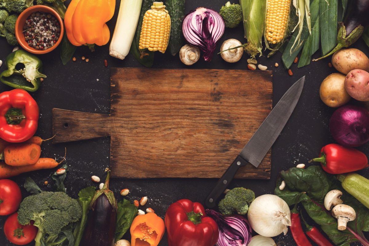 frame of fresh very colourful veg on a wooden background with a chopping board and knife